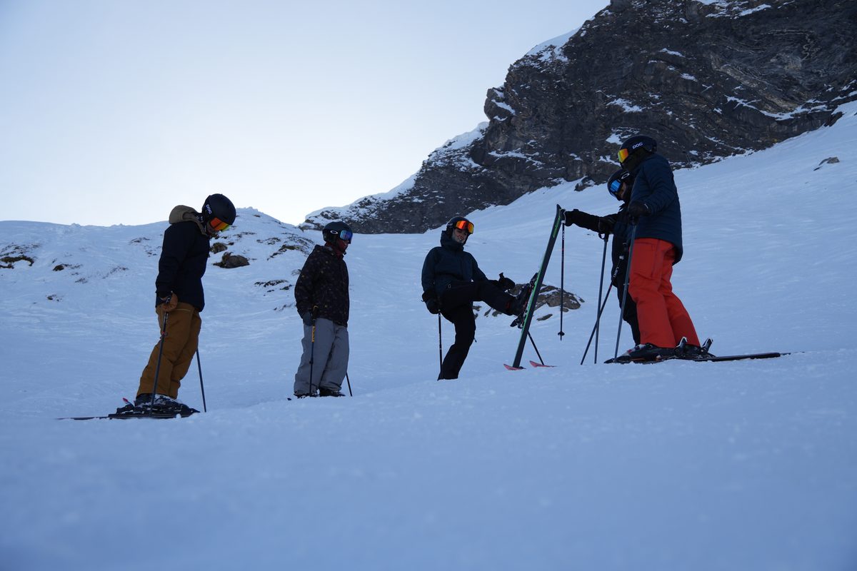 Trainee ski instructors below a rocky alpine face in low evening light